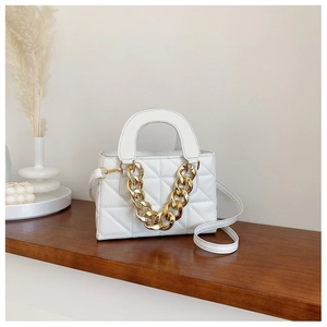 Detail of white quilted handbag with thick gold chain on a wooden shelf in a minimalist setting