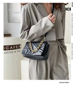 Détail d'un sac bandoulière matelassé noir avec une chaîne dorée dans un café chic