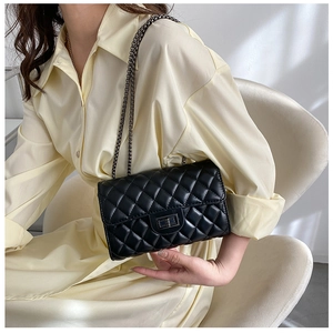 Detail of black quilted leather bag with metallic twist lock and chain strap on a model