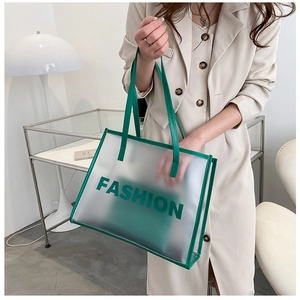 Close-up of clear tote bag with green leather trim and fashion lettering detail