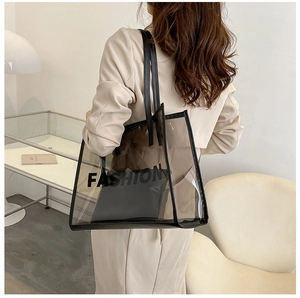 Rear view of model holding a clear PVC tote bag with black trim and a fashion logo