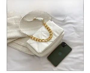 Détail du sac matelassé blanc avec chaîne dorée épaisse à côté d'un smartphone