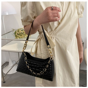 Detail of a black quilted leather shoulder bag with a gold chain strap held by a model