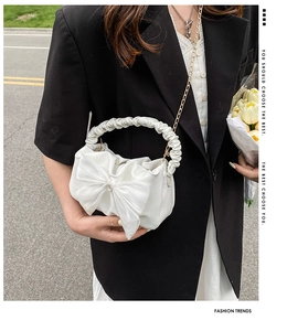 Detail of white bow bag with pleated handle and metal chain shown in outdoor street style