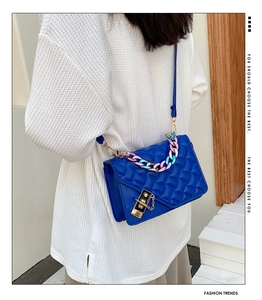 Detail of blue quilted crossbody bag featuring acrylic chain and gold lock on a model