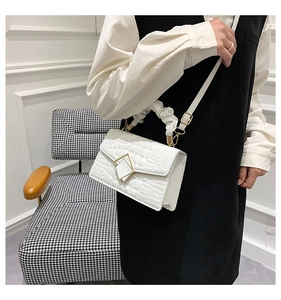 Macro view of white crocodile pattern shoulder bag with gold clasp and ruched handle