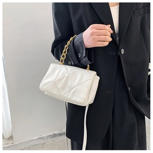 Détail du sac à bandoulière matelassé blanc avec chaîne dorée sur une veste noire