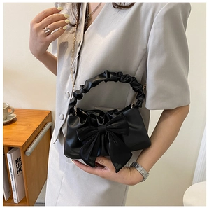 Detail of black pleated cloud bag with oversized bow and elegant gold metal chain