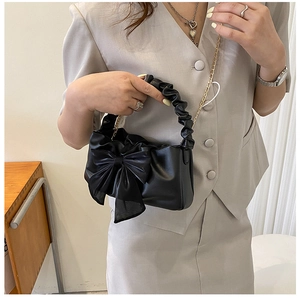 Detail of a black pleated handle bag with a large bow and gold chain strap in use