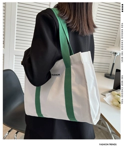 Detailed side view of beige canvas tote bag with green straps and fashion print on bag