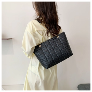 Détail du grand sac cabas matelassé noir avec bandoulière en chaîne dorée porté par un mannequin