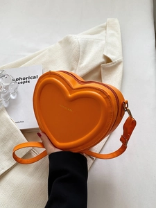 Détail du sac à bandoulière orange en forme de cœur avec texture gaufrée et logo