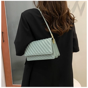 Side view of a mint green quilted crossbody bag with gold hardware worn on a black blazer