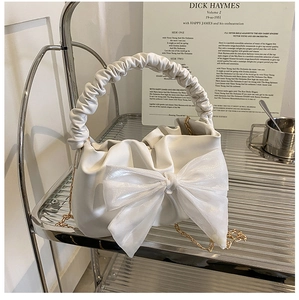 Detail of a creamy white ruched cloud bag featuring a large organza bow and gold chain