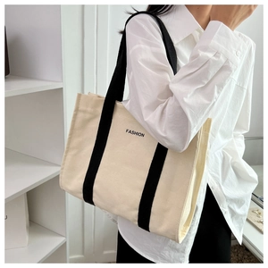 Detail of canvas tote bag showing black FASHION lettering and reinforced shoulder straps