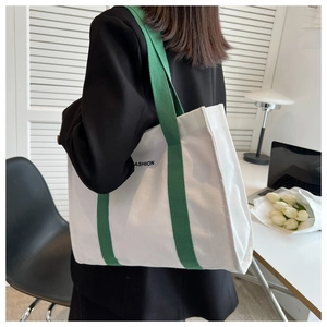 Detailed view of canvas tote bag with green straps worn by model in a cozy indoor setting