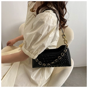 Detail view of black baguette bag with embossed square pattern and gold chain strap