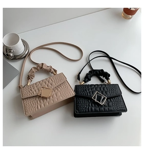 Detail of crocodile embossed crossbody bags in beige and black with pleated handles