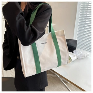 Detail of canvas tote bag with green straps worn by model in a modern office setting