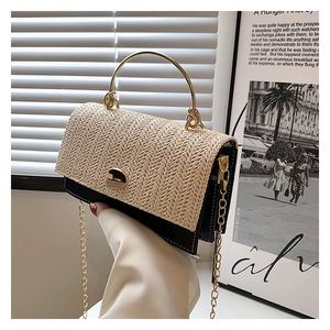 Detailed view of woven straw and black leather crossbody bag with golden chain strap