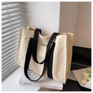 Detail of canvas tote bag with black handles and fashion text in a lifestyle setup