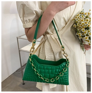 Detail of emerald green quilted baguette bag with chunky gold chain strap on model