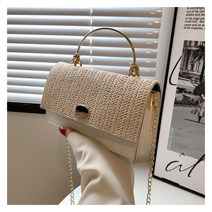 Detail of woven straw flap and gold circular handle on white stylish crossbody bag