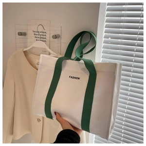 Detailed close-up of a canvas tote bag with green handles and fashion print text