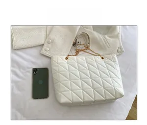 Vue de dessus d'un sac cabas blanc matelassé avec chaîne dorée sur un fond en tissu doux