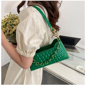 Detail of green baguette bag with embossed diamond texture and gold chain on model