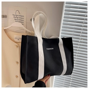 Detail view of the black canvas tote bag showing wide white handles and fashion print
