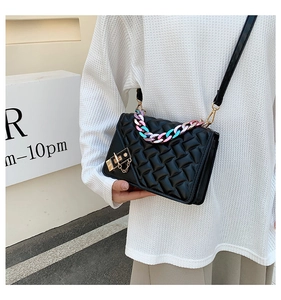 Close-up of black quilted shoulder bag with golden lock and colorful resin chain detail