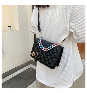 Detail of black woven leather handbag featuring a rainbow chain strap and gold clasp