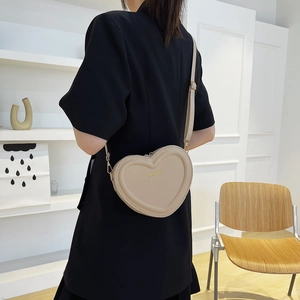 Sac à bandoulière chic en forme de cœur beige porté par un mannequin en intérieur