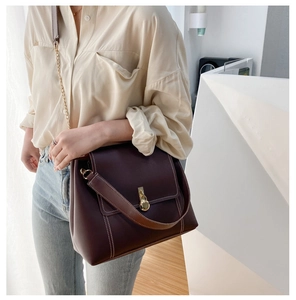 Detail of deep brown tote bag featuring contrast stitching and golden circular lock buckle