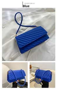 Close-up of blue quilted PU leather small square bag with diagonal stitching and gold metal buckles
