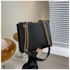 Detail of black crocodile texture shoulder bag with golden chain straps and metal closure