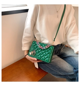 Detail of green quilted crossbody bag with vibrant acrylic chain and gold lock closure