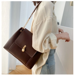 Detail of dark brown leather tote bag with white stitching and gold chain strap