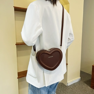 Sac à bandoulière marron en forme de cœur avec finitions dorées sur costume blanc