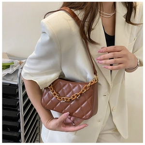 Détail d'un sac bandoulière marron matelassé avec chaîne ambre sur un blazer ivoire