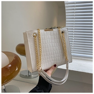 Detail of white crocodile embossed tote bag featuring a gold chain and leather handle