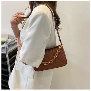 Détail du sac sous le bras matelassé marron avec chaîne or et ambre sur blazer blanc