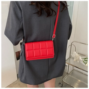 Detail of red quilted square crossbody bag with adjustable strap on grey blazer