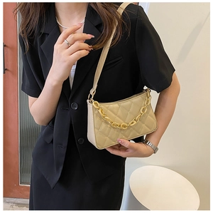 Détail du sac bandoulière beige matelassé avec chaîne dorée sur un blazer noir