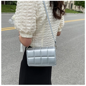 Detail of silver quilted crossbody bag with textured grid patterns and braided strap
