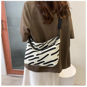 Detail of striped canvas tote bag with black chain and wide shoulder strap on model