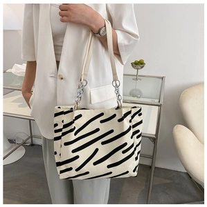 Detail of canvas tote bag showing black stripes, leather straps and silver chain link