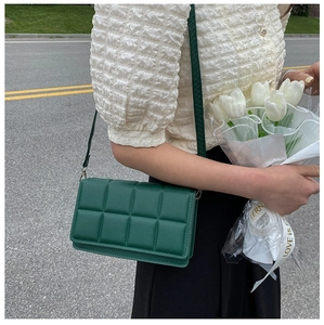 Outdoor model holding dark green padded woven faux leather crossbody square bag