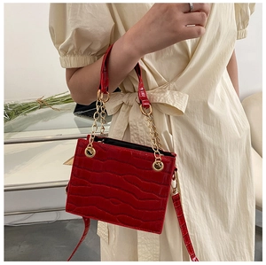 Detail of red croc-effect crossbody bag with gold chain strap on model's shoulder